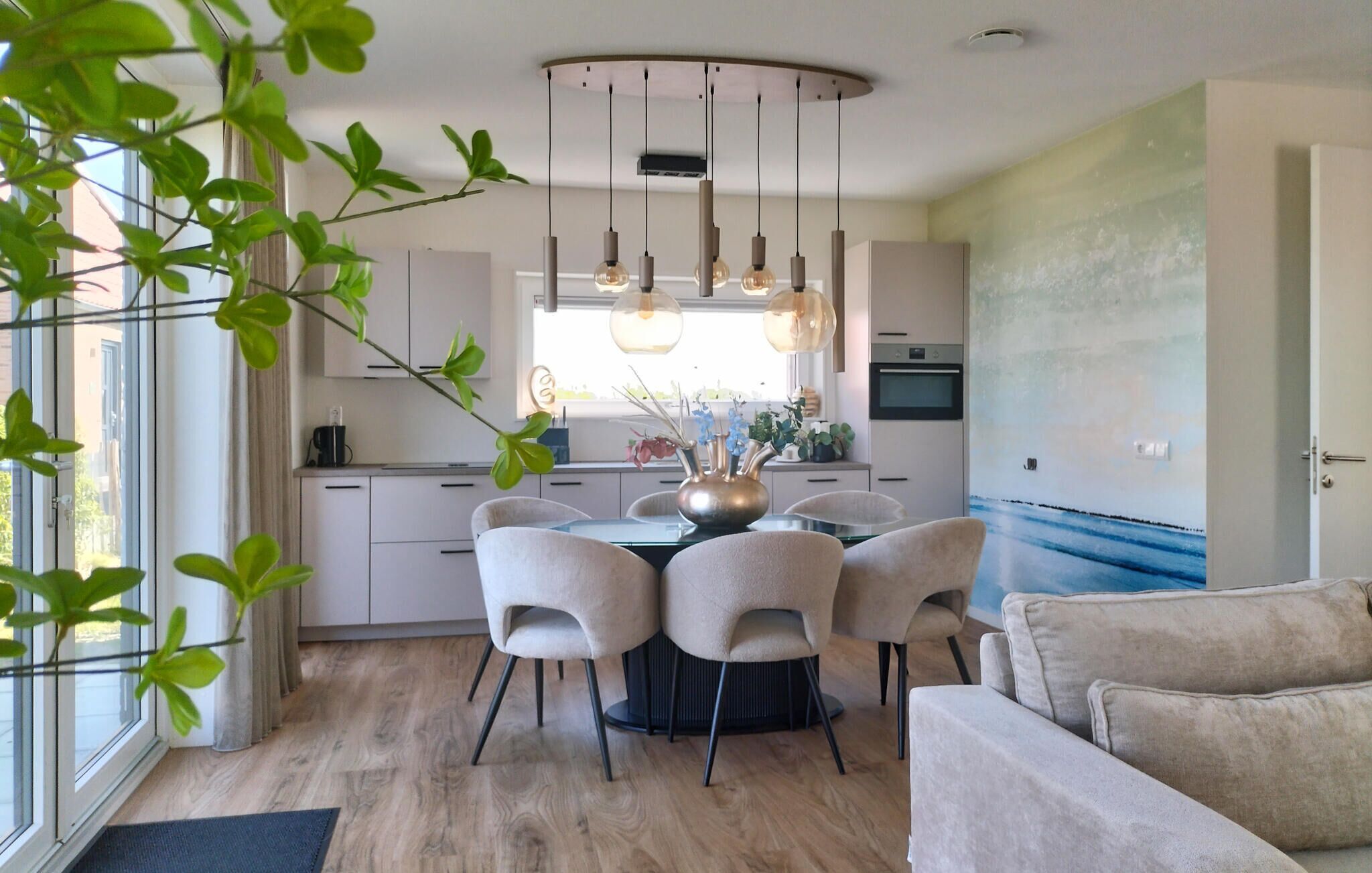 A modern kitchen with a dining table surrounded by chairs, a built-in oven, and a window with curtains.
