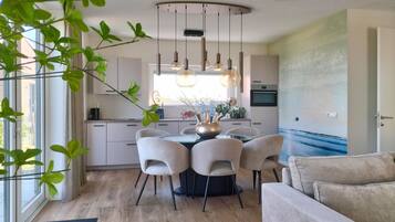 A modern kitchen with a dining table surrounded by chairs, a built-in oven, and a window with curtains.