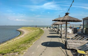 Une promenade en bord de mer agrémentée d’un pavillon à toit de chaume, de chaises longues en bois et offrant une vue sur l’océan.