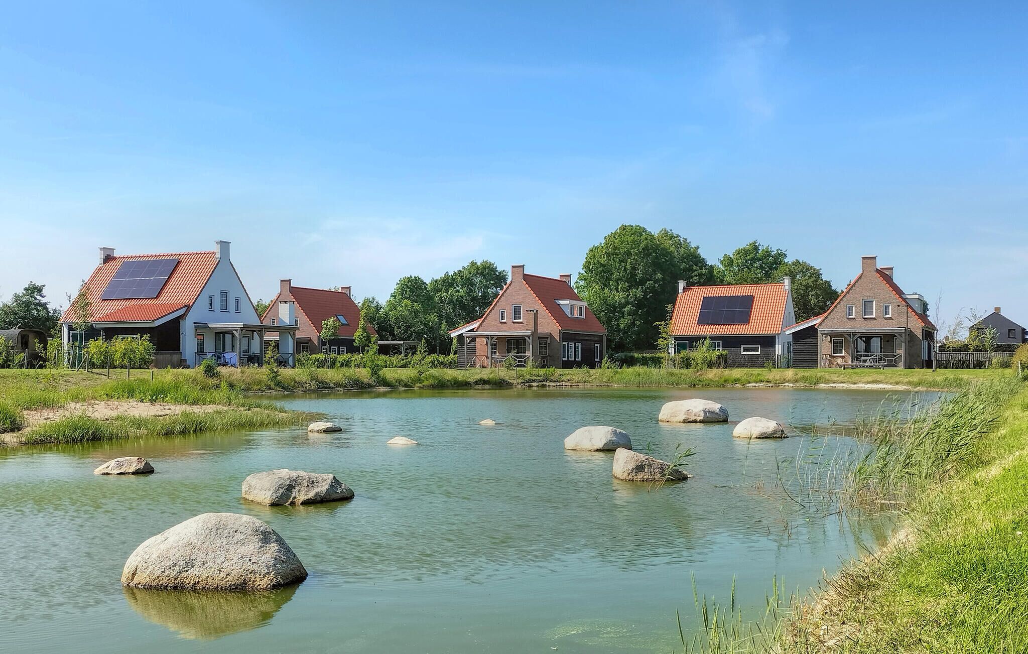A riverside village with traditional houses, a calm river, and large rocks in the water.