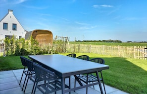 Eine Terrasse mit Tisch und Stühlen, einem Holzfass und einem Haus mit geneigtem Dach.