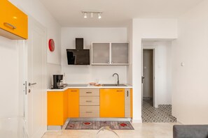 Eine kleine Küche mit orangefarbenen Schränken, einer schwarzen Dunstabzugshaube, einer roten Uhr und einem gemusterten Teppich.