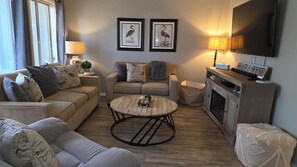 A living room with a sofa, two armchairs, a coffee table, a fireplace, and framed artwork on the wall. - Cozy 2-bedroom condo in Myrtle Beach, Shore 2 Please (Myrtle Beach)