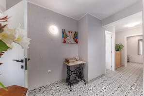 Een gang met een patroon vloer, een tafel met boeken en een schaal, een schilderij aan de muur en een deur met een lamp.