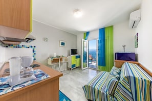 A compact room with a kitchenette, a bed with striped bedding, a desk with a computer, and a view through a glass door. - Beachside Villa Mia Apartment 1, Medveja, Croatia (Medveja)