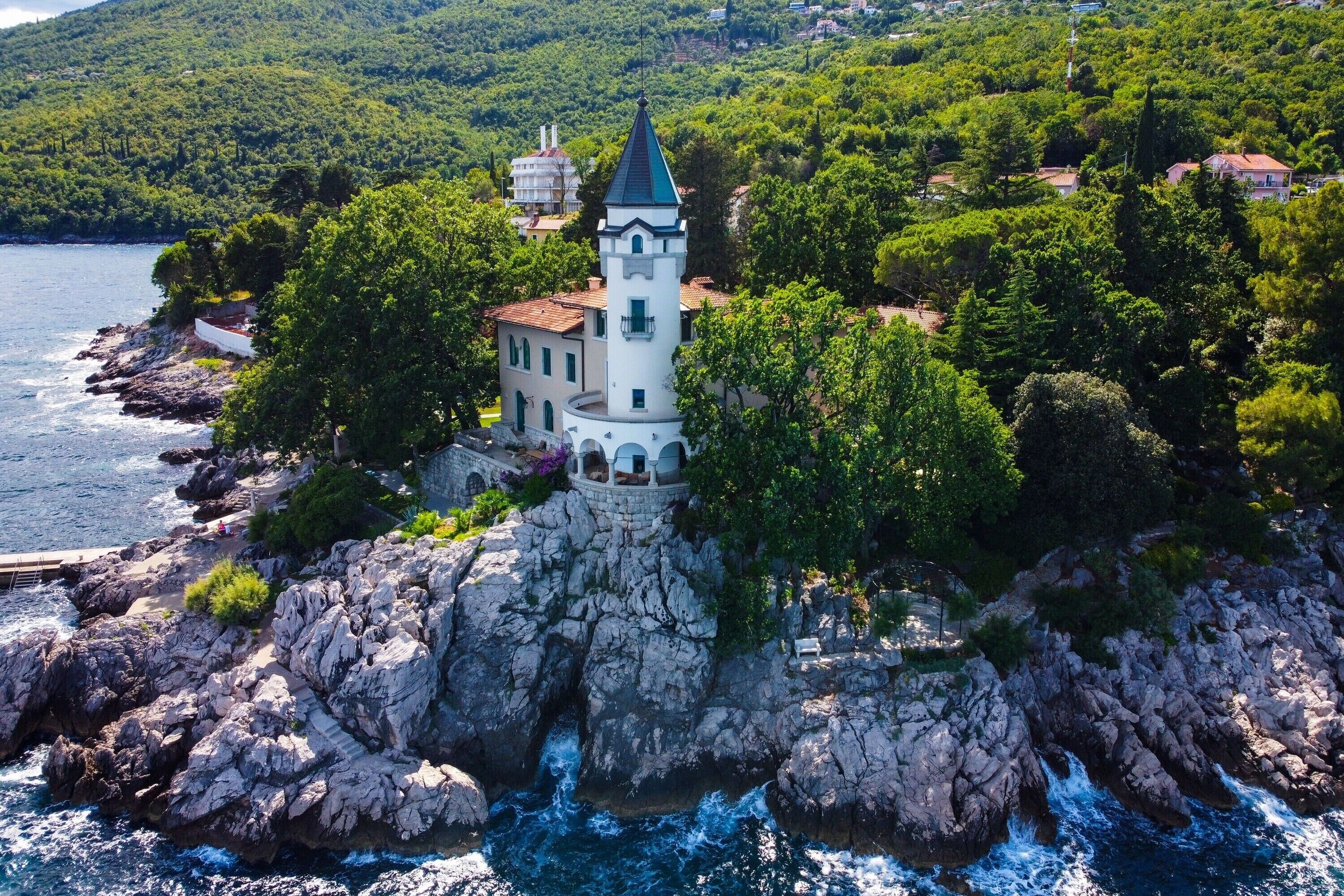 A coastal building with a tower, surrounded by rocky terrain and greenery.