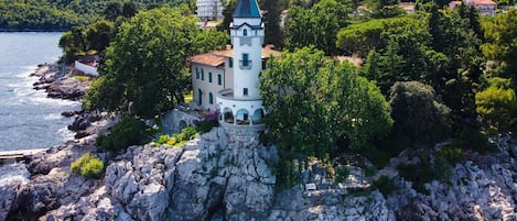 A coastal building with a tower, surrounded by rocky terrain and greenery.