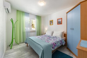 A bedroom with a bed, a wardrobe, a standing fan, and a window with curtains. - Beachside Villa Mia Apartment 1, Medveja, Croatia (Medveja)