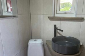 Et badeværelse med toilet, håndvask og et vindue over vasken.