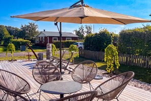 Eine Terrasse im Freien mit Korbmöbeln, einem Tisch und einem Sonnenschirm.