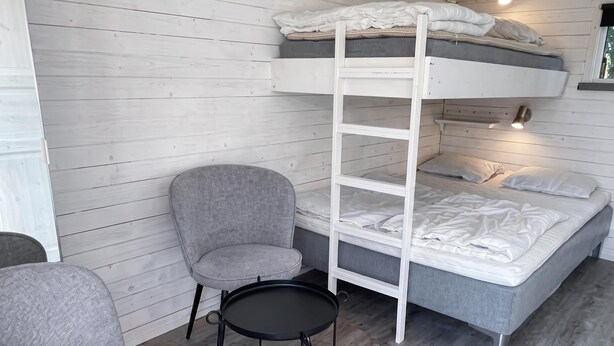 En køjeseng med stige, en grå lænestol, et lille rundt bord og en sengetårnslampe.