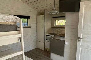 Eine kleine Küche mit Kühlschrank, Herd und Spüle, einem Etagenbett mit Matratze sowie einem Fenster.