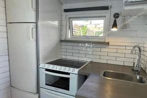 Een kleine keuken met witte apparaten, een raam en een roestvrijstalen spoelbak.