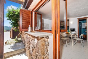 A stone ledge with a wooden door, a dining area with a table and chairs, and a view of the outdoors. - Ladunia 2, Marinella, Italy (Marinella)