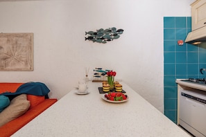 A kitchen with a white countertop, a sink, and a stove. There is a wall-mounted fish decoration and a framed picture. - Ladunia 2, Marinella, Italy (Marinella)