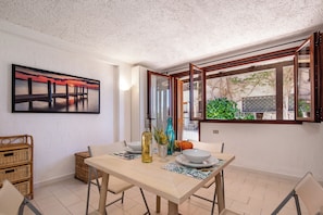 A dining area with a table, chairs, a painting, and a window with a view of greenery. - Ladunia 2, Marinella, Italy (Marinella)