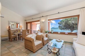A furnished living room with wicker furniture, a dining area, and a large window with a view of the sea. - Casa Titta, Marinella, Italy (Marinella)