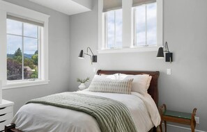 Een slaapkamer met een bed, twee bedlampen, een raam, een nachtkastje en uitzicht op de omgeving.