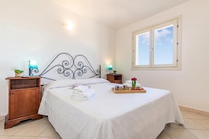 A neatly made bed with white linens, a wooden nightstand with a lamp, a tray with food and flowers, and a window with a view of the sky. - Elicriso, San Pasquale, Italy (San Pasquale)