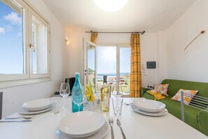A dining area with a table set for two, a view of the sea through a window, and a green sofa with patterned cushions. - Elicriso, San Pasquale, Italy (San Pasquale)