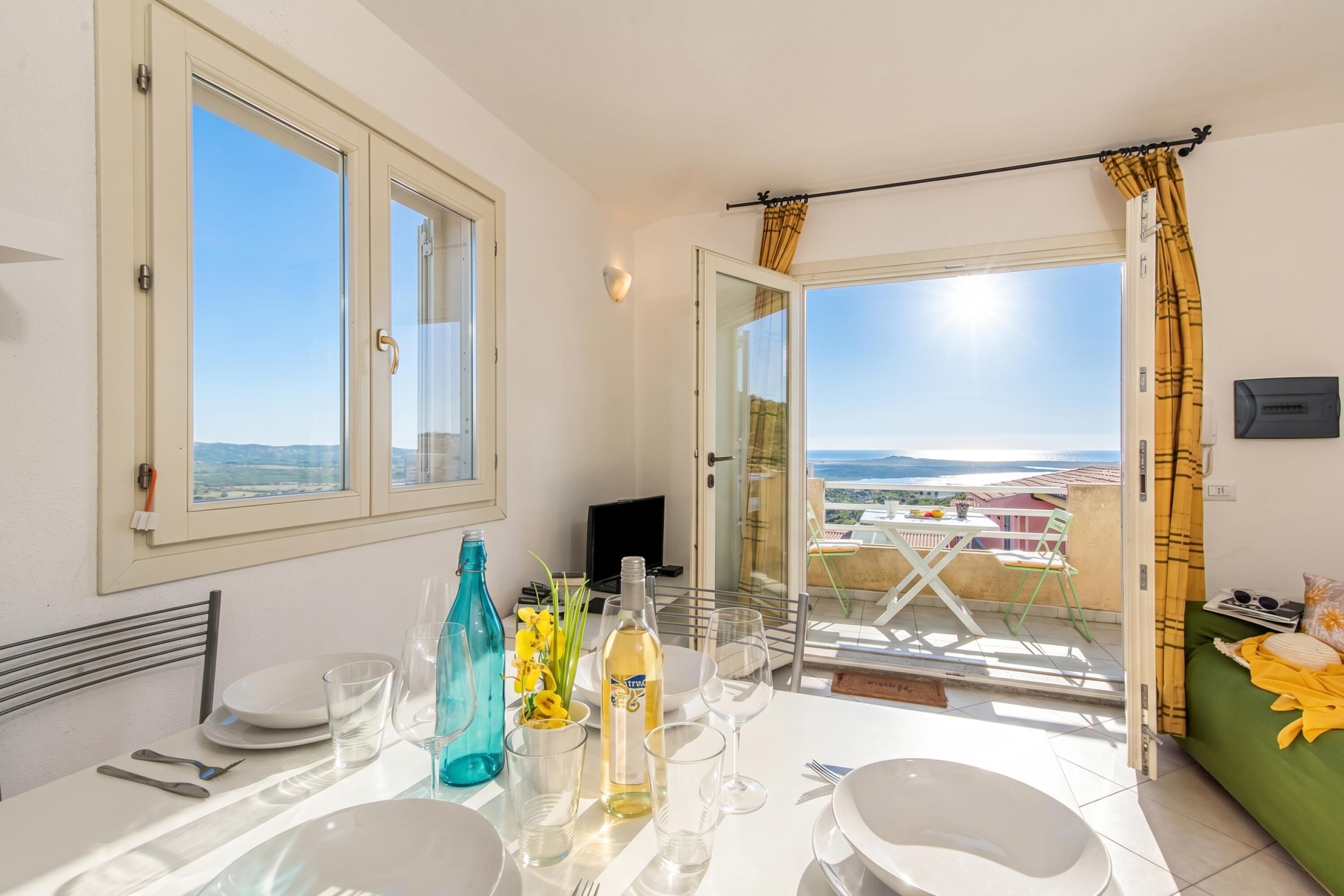 A balcony with a table set for dining, a sofa, and a view of the landscape.