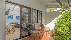 A covered patio with wicker furniture and a sliding glass door leading to an indoor area with a sofa and artwork. - 71 Mandalay : Deluxe Studio (Nelly Bay)