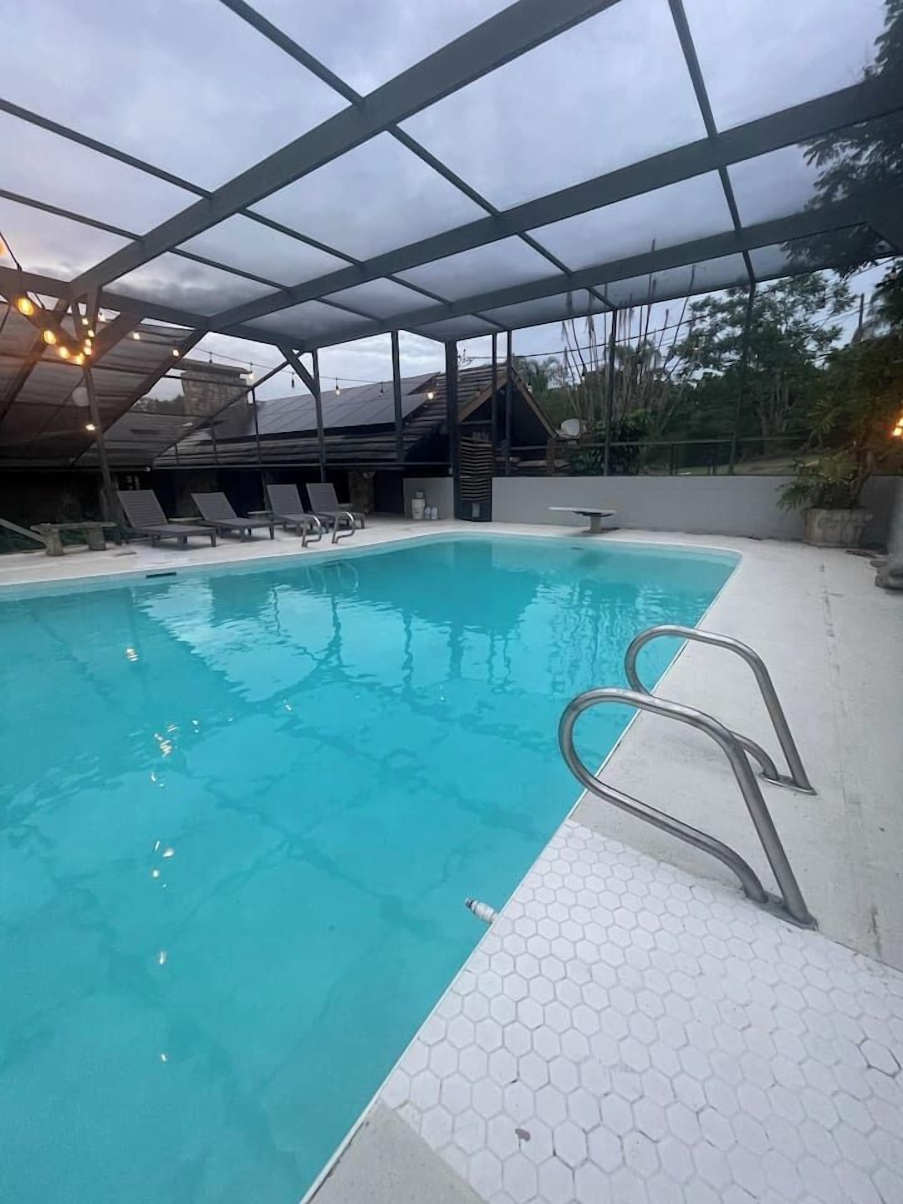 Una piscina con tetto in vetro, circondata da sdraio e un pavimento a mosaico esagonale.