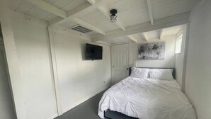Ein Schlafzimmer mit einem Bett, einem Fernseher, einer Tür und einer Deckenleuchte.