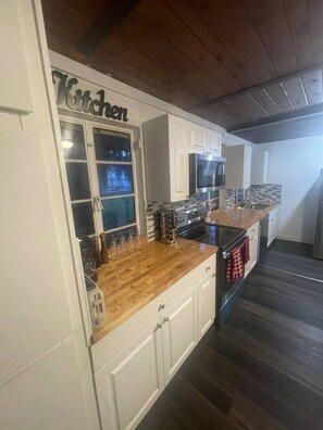 A kitchen with white cabinets, a wooden countertop, a microwave, and a stove.