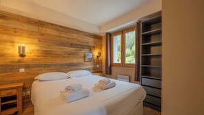 A bedroom with a wooden headboard, a bed with white linens, two wall-mounted lights, a window with curtains, and a built-in shelf unit. - V Balme 26: Beside Ski Lift; Pool, Sauna & Gym, Vallorcine (Argentiere), France (Vallorcine (Argentiere))