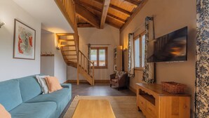 A living room with a sofa, a wooden bench, a staircase, a TV, and a patterned curtain. - V Balme 26: Beside Ski Lift; Pool, Sauna & Gym, Vallorcine (Argentiere), France (Vallorcine (Argentiere))