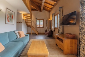 Ein Wohnzimmer mit einer Couch, einer Holzbank, einer Treppe, einem Fernseher und einem gemusterten Vorhang.