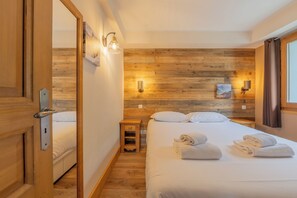 Ein Hotelzimmer mit einer Holzvertäfelung, einem Bett mit weißer Bettwäsche, zwei Nachttischen mit Lampen und einem Fenster mit Vorhängen.