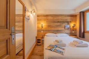 Habitació d'hotel amb paret de fusta, un llit amb roba blanca, dues taules de nit i una finestra amb cortines.