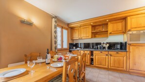 Un coin repas avec une table en bois dressée pour deux personnes, une cuisine avec des placards en bois et un four encastré.