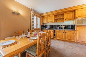 Ein Essbereich mit Holztisch, gedeckt für zwei Personen, eine Küche mit Holzschränken und einem eingebauten Backofen.