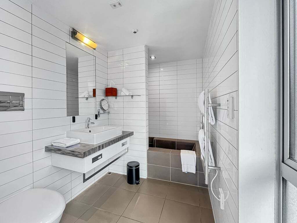A modern bathroom with white tiles, a sink, mirror, and a shower area.