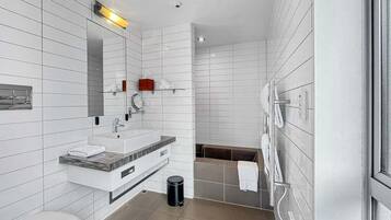 A modern bathroom with white tiles, a sink, mirror, and a shower area.