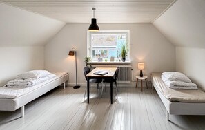 A dorm-style room with two single beds, a small table, a chair, a standing lamp, a window with a view of a street, and a radiator. - Beautiful home in Allinge with WiFi (Allinge)