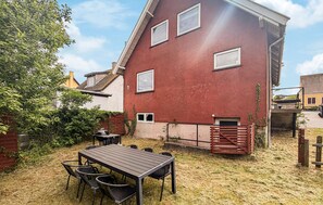 Ein rotes Gebäude mit einem geneigten Dach, einer Terrasse mit Tisch und Stühlen sowie einem eingezäunten Bereich.