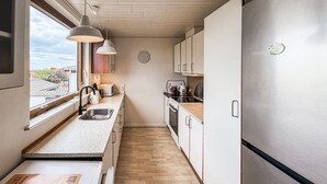 Eine kompakte Küche mit Spüle, Herd und Kühlschrank, Holzboden und Pendelleuchten.