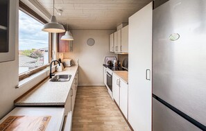 Eine kompakte Küche mit Spüle, Herd und Kühlschrank, Holzboden und Pendelleuchten.