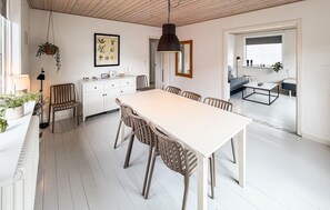 Ein Essbereich mit einem weißen Tisch und Stühlen, einer hängenden Pflanze und einem gerahmten Pflanzenbild an der Wand.