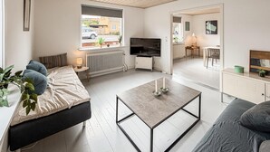 Ein modernes Wohnzimmer mit einer Couch, einem Couchtisch, einem Fernseher und einem Essbereich mit Tisch und Stühlen.