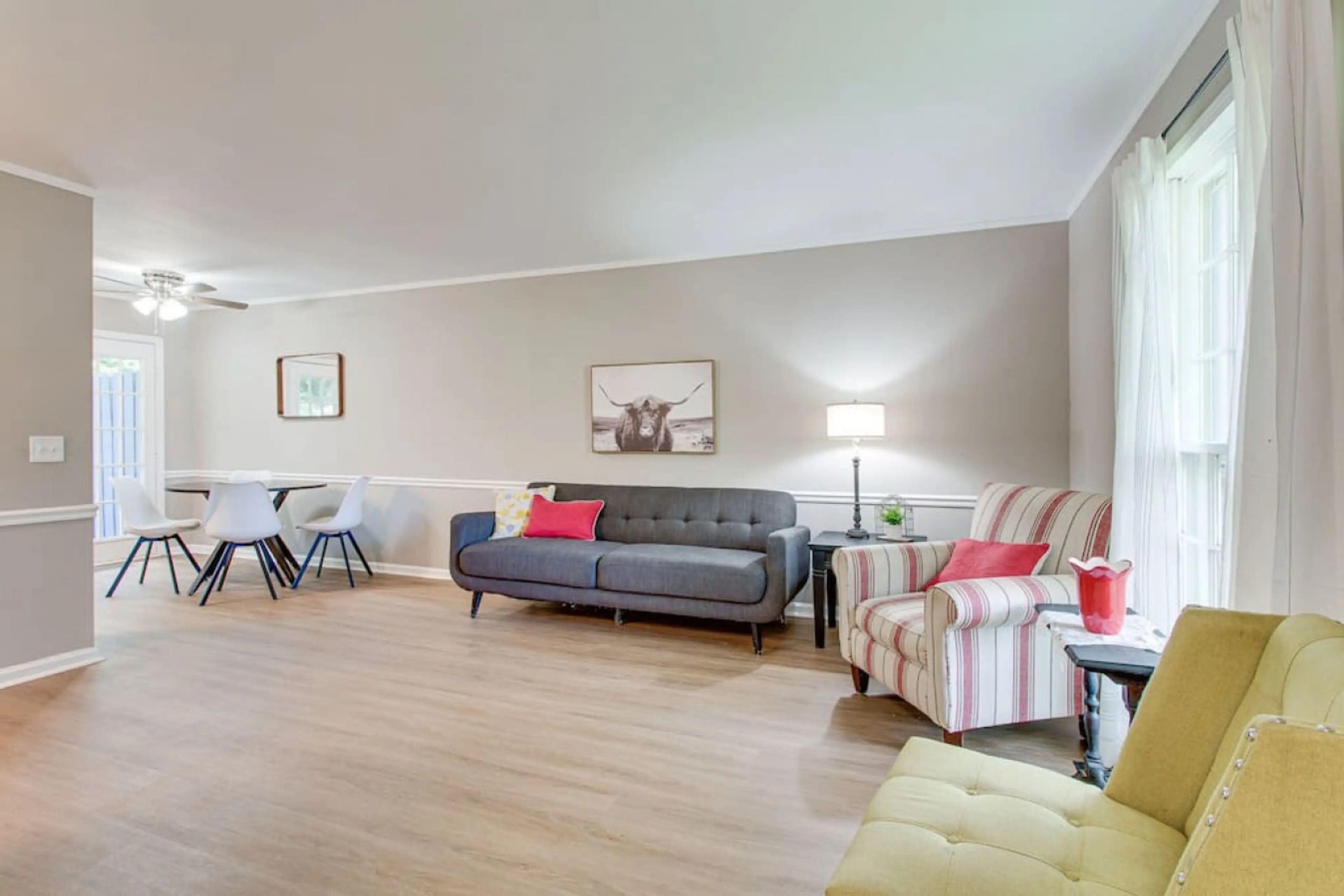 A living room with a grey sofa, striped armchairs, a dining table with chairs, and a ceiling fan.