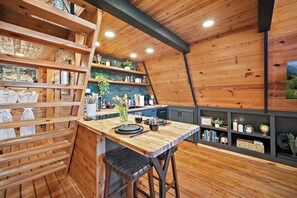 Een knus, houten interieur met een eethoek, een bar en planken met diverse spullen.