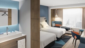 A modern hotel room with two beds, a desk, a chair, a window with a city view, and a bathroom with a sink and mirror.