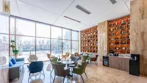 A modern hotel lobby with large windows, a seating area, and a bookshelf.