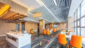 A modern hotel lobby with a marble floor, orange and white chairs, a reception desk, and large windows.