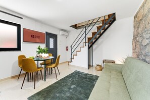 A modern living room with a staircase, a dining area with chairs and a table, and a green sofa. - GuestReady - Courtyar 9/99 - Apt 05 (Porto)